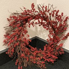 a wreath made out of branches and berries on a black countertop next to a white wall