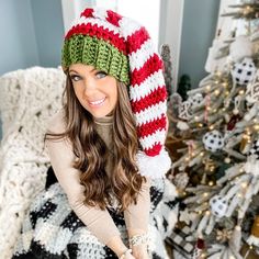 a woman wearing a knitted christmas hat sitting in front of a decorated christmas tree