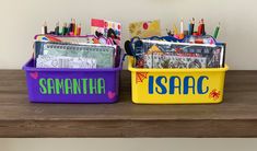 two plastic containers filled with school supplies on top of a wooden shelf next to each other