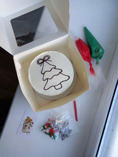 a white cake in a box with a christmas tree on it and some candies