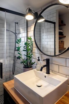 a white sink sitting under a bathroom mirror next to a wooden counter topped with a potted plant