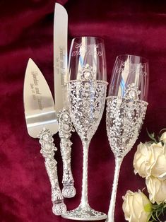 three wine glasses sitting next to each other on a red velvet tablecloth with white roses