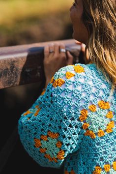 a woman wearing a blue crochet sweater holding a wooden slatted bench