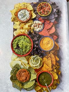 an open book with different types of dips and chips in bowls on it next to a bowl of guacamole