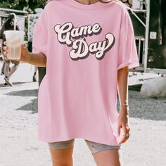 Make a statement with our retro game day t-shirt! Made with high-quality, comfortable fabric, this shirt is ideal for lounging on game day or heading out with friends. Get ready to turn heads with this fun and trendy addition to your wardrobe. Comfort Colors Garment Dyed 1717 Unisex Short Sleeve T-Shirt Relaxed fit, please check the size chart in photos to ensure the correct size.  100% Ring Spun Cotton Pre-Shrunk Fabric for size retention Care Instructions:  Machine wash cold inside out, Tumble Pink Crew Neck T-shirt For Game Day, Retro Game Day T-shirt With Team Name, Retro Team Name T-shirt For Game Day, Game Day Fan Apparel T-shirt With Slogan, Retro Game Day Tops With Text Print, Retro Tops With Text Print For Game Day, Pink Letter Print Tops For Game Day, Retro Letter Print T-shirt For Game Day, Graphic Tee Crew Neck Shirt For Game Day