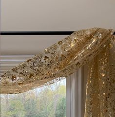 an open window with gold curtains in front of it and trees outside the windowsill