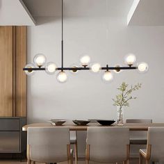 a dining room table and chairs with lights hanging from the ceiling above it, in front of a white wall