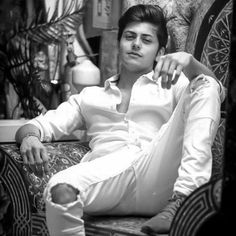 a young man sitting on top of a chair next to a plant and lamp shade