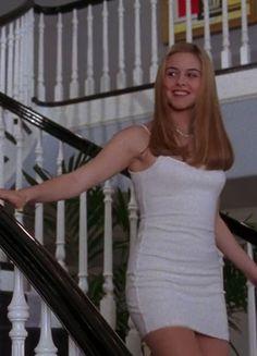 a woman in a white dress is walking down the stairs with her hand on the railing