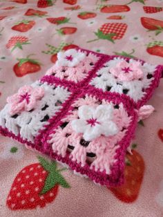 a pink and white crocheted object laying on top of a bed covered in strawberrys