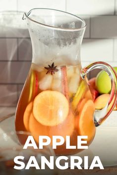 a pitcher filled with liquid sitting on top of a counter next to apples and oranges