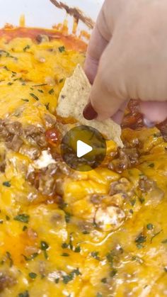 someone dipping a tortilla chip into a casserole dish with cheese and meat