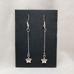 silver earrings with stars hanging from them on a black card board, against a white background