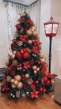 a christmas tree decorated with red and gold ornaments in a living room next to a lamp post