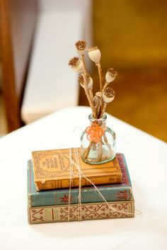 two books stacked on top of each other with flowers in a vase sitting on top of them