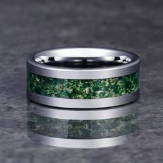 a wedding ring with green and white marble inlays on it, sitting on a gray surface