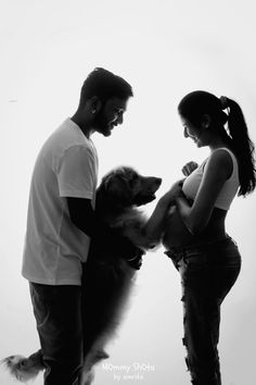 a man and woman standing next to each other with a dog on their lap in front of them