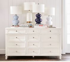 two lamps on top of a white dresser with blue and white vases in the background