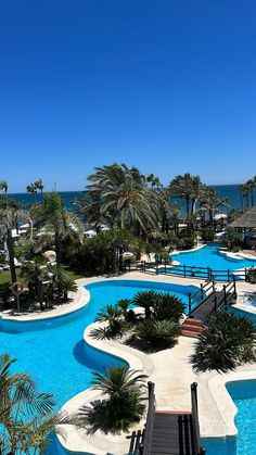 an outdoor swimming pool surrounded by palm trees and water features blue skies, white sand and the ocean in the background