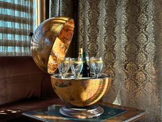 a globe with wine glasses in it on a table next to a curtained window