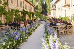 people are sitting at tables in the middle of an alleyway lined with flowers and greenery