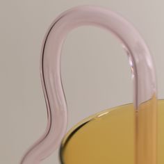 a yellow glass vase with a curved handle on it's side and the bottom half filled with liquid