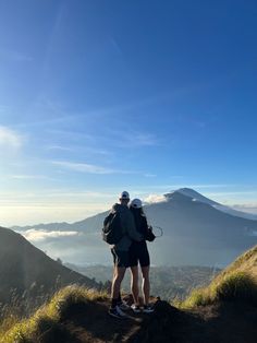 two people standing on top of a mountain looking out at the clouds and mountains in the distance