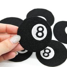 a hand holding a black and white number eight ball sticker on top of four other black and white numbers