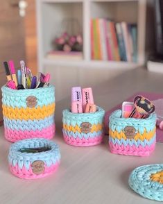 there are some crochet baskets on the table with pens and pencils in them