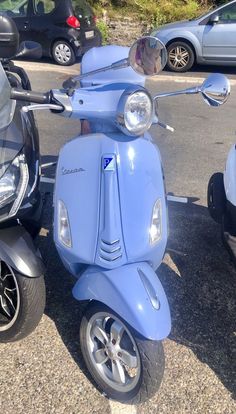 a blue scooter is parked in a parking lot next to two other motorcycles