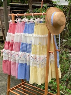 several different colored skirts hanging on a clothes rack with a straw hat resting on it