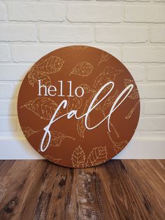 a wooden sign that says hello fall on the side of a white brick wall and wood floor