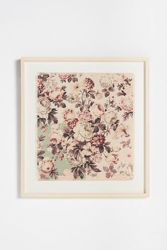 a floral print hangs on the wall above a white framed artwork piece with a wooden frame