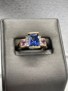 A beautiful ladies multi-gemstone ring designed and made in 10 karat solid yellow gold.  Set with a 2.5 carat rectangular cut Tanzanite stone bordered on each side with four fine white round Diamonds and two princess cut Pink Topaz set one on each side. This is an unusual composition of colored stones that always looks amazing and drips with sparkle. Weight:  4.2 grams Size:  7 ½  Our Price $595.00 Regularly Priced At $900.00 Please See Our Video Remember - If you're purchasing for yourself or a Formal Rectangular Fine Jewelry Gemstones, Formal Multi-stone Emerald Cut Sapphire Ring, Luxury Rectangular Diamond Ring With Accent Stones, Emerald Cut Multi-stone Sapphire Ring With Diamonds, Emerald Cut Three Stone Birthstone Ring For Formal Occasions, Emerald-cut Sapphire Ring With Gemstone Accents, Emerald Cut Sapphire Ring With Gemstone Accents, Formal Three-stone Emerald-cut Birthstone Ring, Formal Three Stone Emerald Cut Birthstone Ring