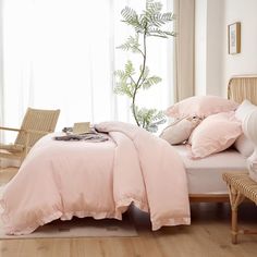 a bed with pink comforters and pillows in a white room next to a window