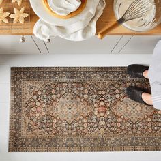 a person standing in front of a rug on top of a wooden table next to a bowl of doughnuts