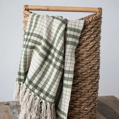 a green and white checkered blanket sitting on top of a wooden table next to a wicker basket