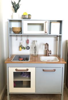 a toy kitchen with sink, cupboards and utensils