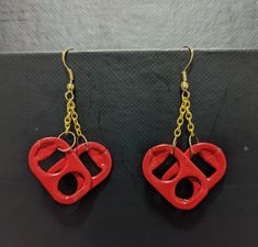 pair of red heart shaped earrings hanging from gold - plated hooks on black surface