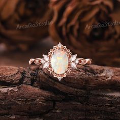 an opal and diamond ring sitting on top of a piece of wood with pine cones in the background