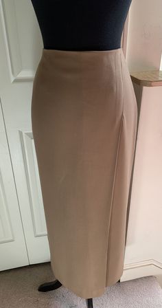 Simply styled with a clean line, this slim skirt has a single, 4" deep, offset front pleat, and a 16" deep back vent for ease in walking. 98% wool, 2% spandex, skirt has a gorgeous, fluid drape. Invisible back zip and hook close. Fully lined, size 4, color Camel. Never worn.  Dimensions: Waist 27" circumference  Hip 37" circumference  35" garment length waist to hem Classic Fitted Midi Skirt, Solid Color Fitted Pleated Skirt, Fitted High Waist Solid Color Skirt, Fitted High Waist Solid Skirt, High Waist Fitted Solid Color Skirt, Elegant Formal Pleated Skirt With Stretch, Elegant High Waist Fitted Skirt, Stretch Full Length Pencil Skirt For Work, Fitted Maxi Skirt For Office