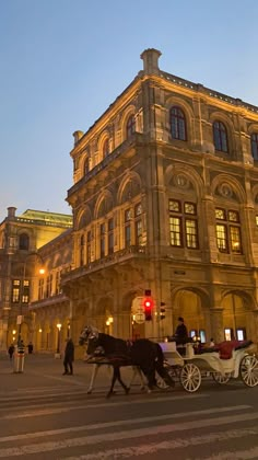 a horse drawn carriage in front of an old building at night with people walking around