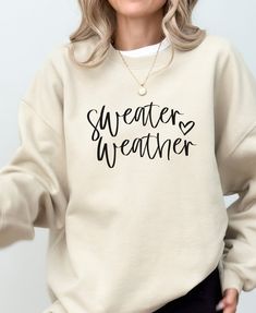 a woman wearing a sweatshirt with the words sweaters weather written on it in black ink