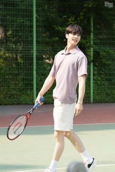 a young man holding a tennis racquet on top of a tennis court next to a ball