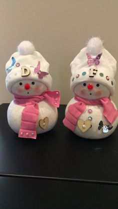 two snowmen wearing hats and scarves on top of a black table next to a wall