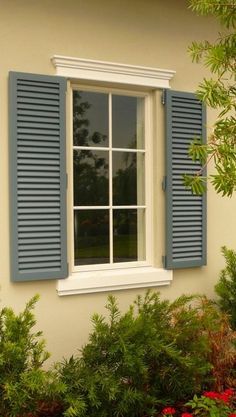 an open window with blue shutters and red flowers in the foreground next to it