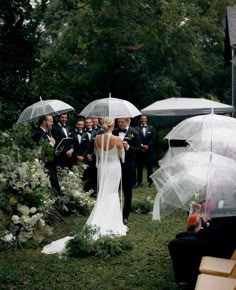 the bride and groom are standing under umbrellas in the rain, surrounded by their wedding party