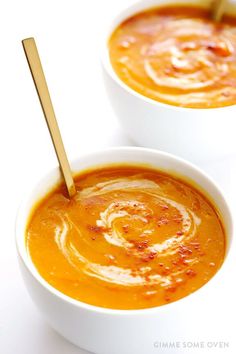 two white bowls filled with carrot soup and topped with a wooden spoon in the middle