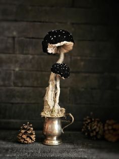 two mushrooms sitting on top of a metal cup next to pine cones and twine