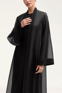 Elevate your wardrobe with the Estee Viscose Open Abaya in Black. Crafted from luxurious viscose, this stunning abaya features elegant flare sleeves and a unique sheer design with solid viscose trim. Breathable and luxurious, this abaya will be your new go-to for sophisticated and exclusive style. Model is 5'7" and is wearing size XS/58". Black Silk Abaya, Arabic Abaya Designs Black, Elegant Black Abaya, Black Abaya Outfit Ideas, Open Abaya Designs, Abaya Fashion Black, Abaya Sleeves, Modest Fashion Aesthetic, Open Abaya Style